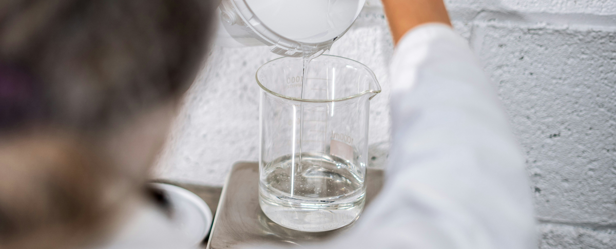 Un liquido trasperente viene versato in un beker grande di vetro per essere pesato.